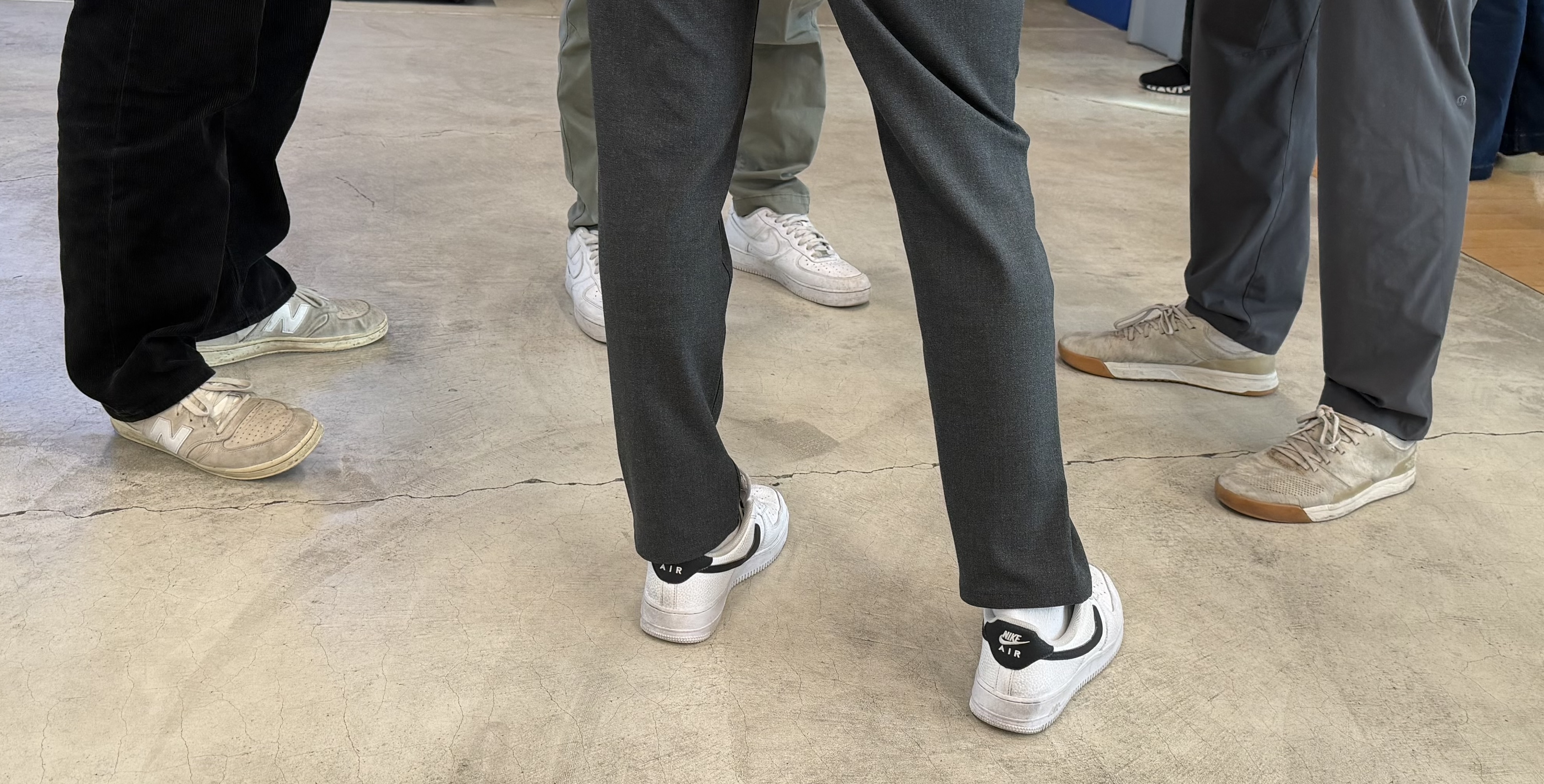 Looking down at a circle of four pairs of worn-in sneakers and boots on a concrete floor.